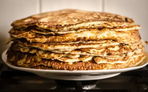 Montón de deliciosos pancakes sin gluten, dorados y esponjosos, apilados en un plato blanco.