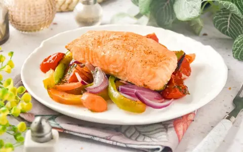 Un jugoso salmón al horno reposa sobre una cama de verduras asadas: tomates, pimientos y cebolla morada.