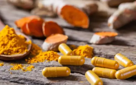 Cápsulas amarillas y polvo de cúrcuma sobre madera rústica, destacando los beneficios de la curcuma en capsulas.