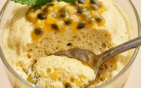Delicioso mousse de maracuyá en vaso, coronado con pulpa y semillas de la fruta, y una hoja de menta. Una cucharada lista para disfrutar.
