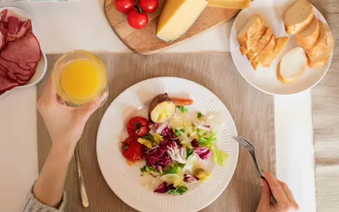Persona disfrutando una ensalada, tomates, patata asada y un vaso de zumo, parte de su dieta intermitente 16/8.