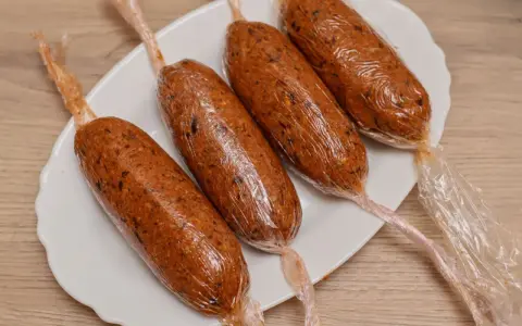 Cuatro chorizos veganos envueltos en plástico transparente, listos para cocinar.