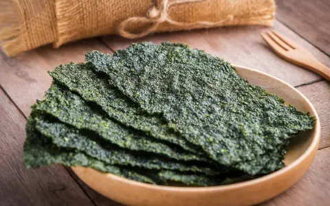 Plato de madera con finas láminas de varios tipos de algas comestibles, listas para disfrutar.
