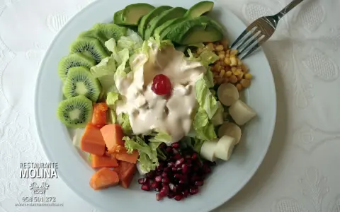 Ensalada tropical con aguacate, kiwi, papaya, palmitos, maíz y granada, cubierta de aderezo cremoso y una cereza.