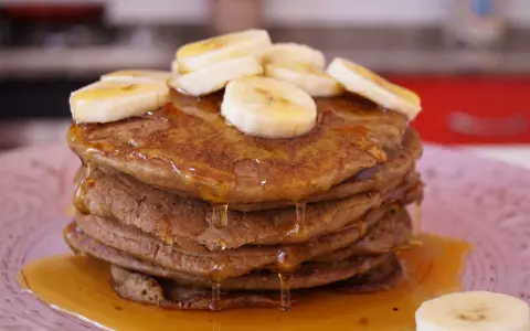 Pila de tortitas de avena y plátano, cubiertas con rodajas de plátano y sirope dorado. ¡Un desayuno delicioso!