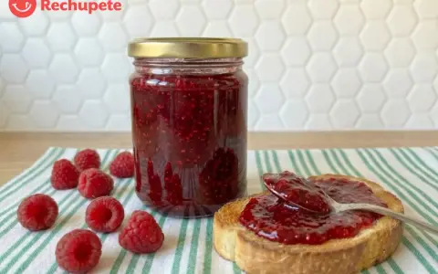 Tarro de mermelada de frambuesa casera, con frambuesas frescas y una tostada untada.