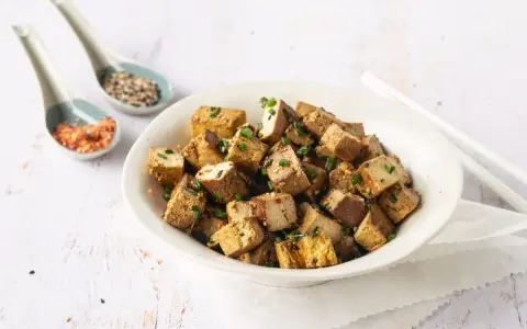Tazón lleno de cubos dorados de tofu marinado, espolvoreados con cebollín y semillas.