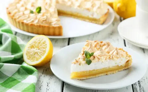 Un delicioso pastel de limón con merengue dorado, acompañado de limones frescos y una servilleta a cuadros verdes. Los ingredientes del lemon pie lucen perfectos.