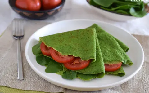 Deliciosos crepes de espinacas rellenos de rodajas de tomate fresco y hojas de espinaca, servidos en un plato blanco.