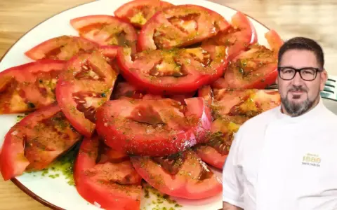 Un chef sonriente presenta un plato de tomate aliñado, fresco y jugoso, con un aderezo verde y aceite.