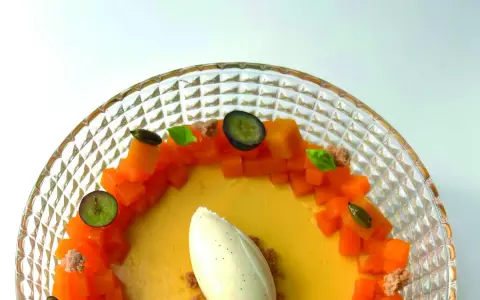 Delicioso flan de mango con helado de vainilla, trozos de mango fresco, arándanos y hojas de menta en un plato de cristal.
