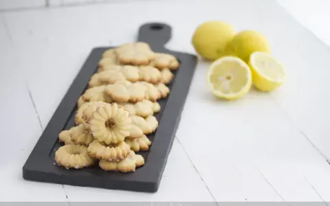 Deliciosas galletas de limón dispuestas en una tabla negra, con limones frescos al lado.
