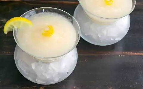 Dos copas de sorbete de limón, una con rodaja de limón y rizo de piel, servidas sobre hielo picado.
