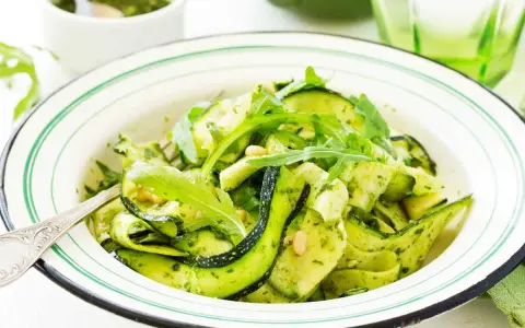 Deliciosa ensalada de calabacín en espiral con pesto y rúcula, adornada con piñones. Un plato fresco y vibrante.