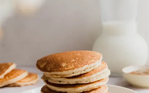 Una pila de esponjosos **pancakes de avena** dorados, con un jarro de leche y un tazón de canela al fondo.