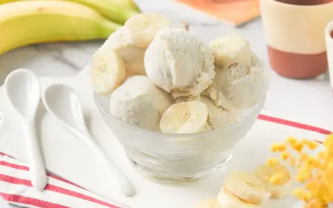 Delicioso helado de platano casero, cremoso y refrescante, servido en un cuenco de cristal con rodajas de plátano fresco.