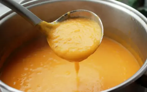 Cucharón sirviendo una deliciosa crema de zanahoria y puerro recién hecha de una olla.
