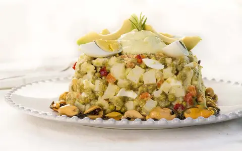 Deliciosa ensaladilla de aguacate con huevo duro, guisantes y mejillones, coronada con una crema suave y rodajas de aguacate fresco.