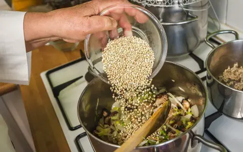 Mano añade trigo sarraceno a una olla con verduras y champiñones.