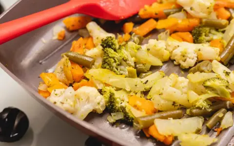 Coliflor al ajillo salteada con brócoli, zanahoria y judías verdes en una sartén, lista para servir.