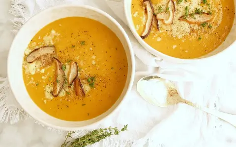 Dos tazones de cremosa sopa de calabaza, adornados con champiñones y queso rallado, listos para ser disfrutados.
