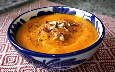 Crema de zanahoria y jengibre, servida en un cuenco azul y blanco, adornada con nueces y pimienta.