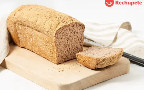 Pan sin gluten recién horneado, con una rebanada lista para disfrutar. Su textura porosa y corteza dorada invitan a probarlo.