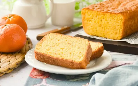 Un delicioso bizcocho de mandarina, recién horneado, con dos rebanadas servidas en un plato blanco.