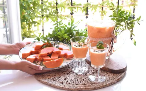 Delicioso zumo de papaya servido en copas y jarra, acompañado de papaya fresca en rodajas.