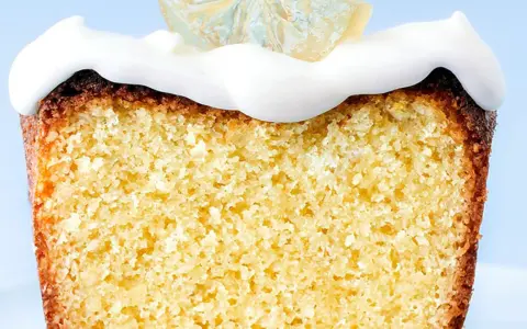 Rebanada de bizcocho esponjoso con un delicioso frosting de limón y una rodaja de limón cristalizado encima.