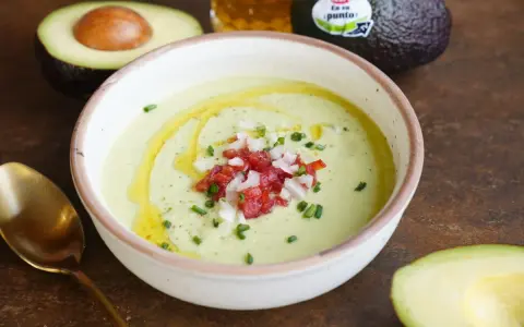 Un cremoso gazpacho de aguacate, adornado con tomate picado, cebolla y cebollino, con un chorrito de aceite de oliva.