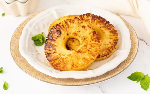 Dos rodajas de piña a la plancha, doradas y caramelizadas, servidas en un plato blanco con hojas de menta.