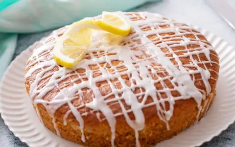 Pastel redondo con glaseado de limón y rodajas de limón fresco.