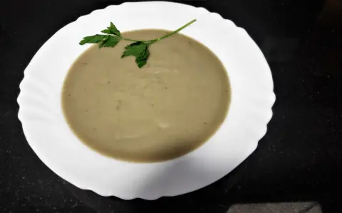 Crema de berenjena suave y sedosa, decorada con una ramita de perejil fresco, lista para disfrutar.