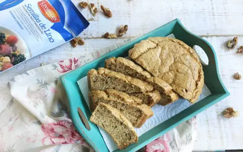 Rebanadas de pan de lino en una bandeja turquesa, junto a un paquete de semillas de lino y nueces.
