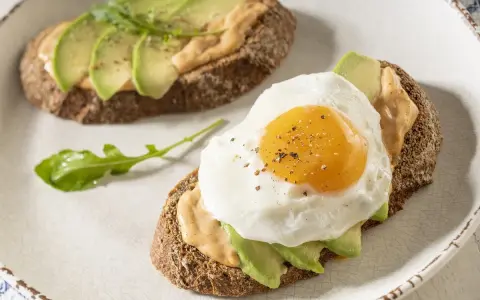 Tostas de aguacate para cenar, una con huevo frito y la otra con rúcula. Delicioso y saludable.