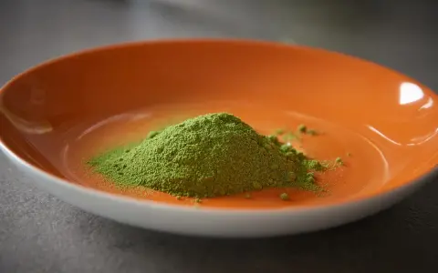 Montículo de polvo verde vibrante, polvo de moringa, en un plato naranja brillante.