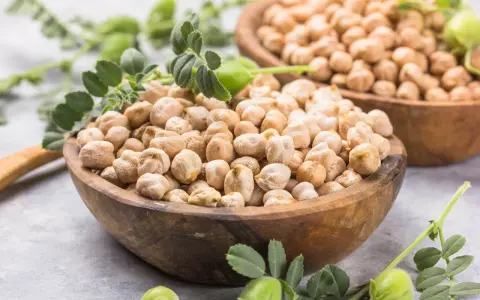 Dos cuencos de madera llenos de garbanzos secos, con hojas verdes y vainas. Los garbanzos tienen fibra, ¡un alimento saludable!