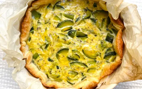 Quiche de calabacín recién horneada, con masa dorada y relleno cremoso salpicado de trozos verdes.