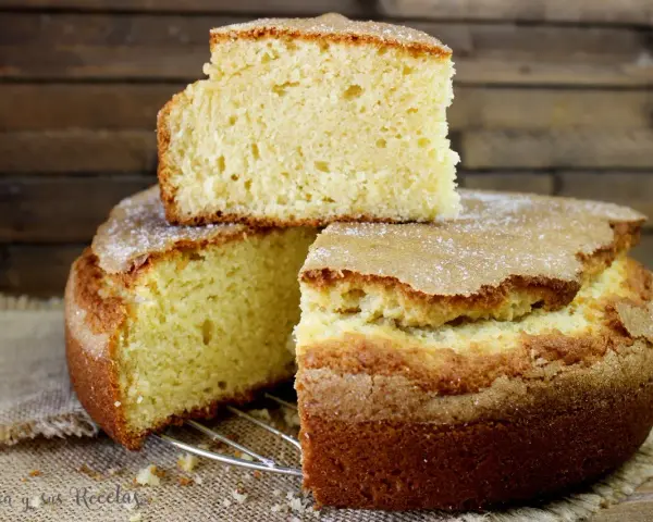 El bizcocho de limón de la abuela, esponjoso y dorado, con una capa de azúcar espolvoreada. Un trozo descansa sobre el pastel principal.