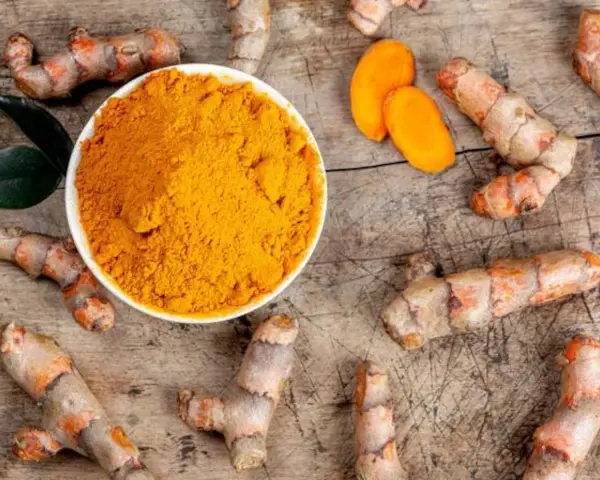 Raíces de cúrcuma y polvo dorado en un cuenco. Descubre qué es la cúrcuma y para qué sirve, un tesoro natural.