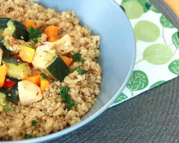 Un tazón de quinoa con pollo y verduras salteadas, como calabacín y zanahoria.