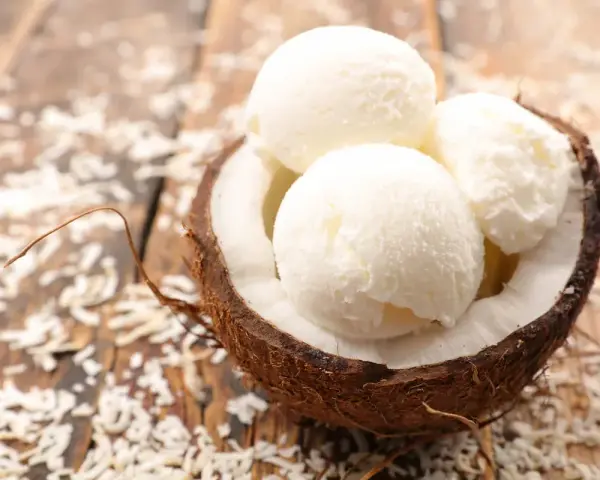 Delicioso helado con leche de coco servido en una cáscara de coco, espolvoreado con coco rallado sobre una mesa de madera.