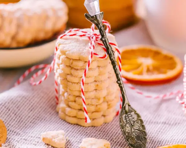 Deliciosas galletas de naranja, apiladas y atadas con hilo rojo y blanco. Una rodaja de naranja y una cuchara antigua completan la escena.