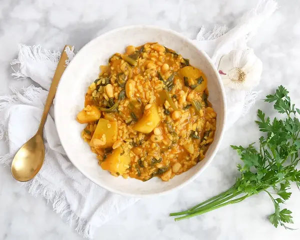 Un tazón de arroz con acelgas, patatas y alubias blancas, servido con una cuchara dorada y perejil fresco.