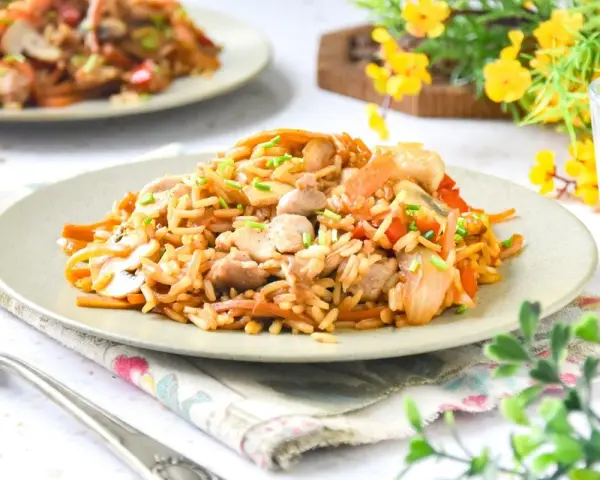 Un delicioso wok de verduras y arroz con trozos de pollo y champiñones, adornado con cebollino fresco.