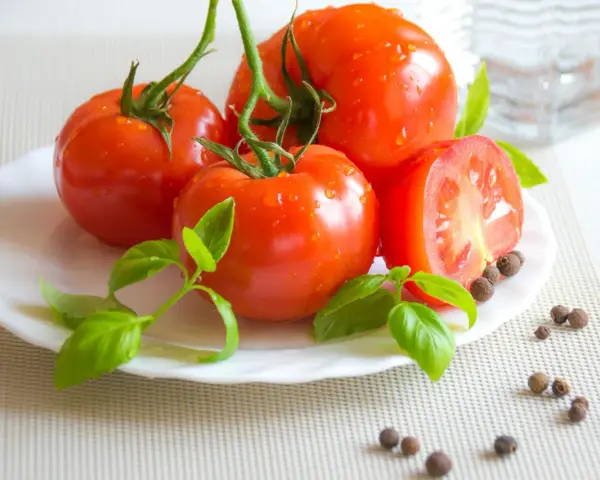 Tomates frescos con gotas de agua, albahaca y granos de pimienta, ingredientes naturales para productos antiinflamatorios.