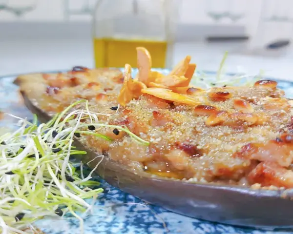 Deliciosa berenjena rellena gratinada, adornada con piñones y brotes frescos, lista para ser disfrutada.