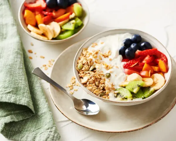 Un tazón de yogur cremoso con granola crujiente, arándanos, fresas, plátano, kiwi y melocotón.