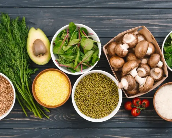 Variedad de alimentos ricos en proteinas vegetales: aguacate, hinojo, lentejas, champiñones, arroz, tomates y hojas verdes.
